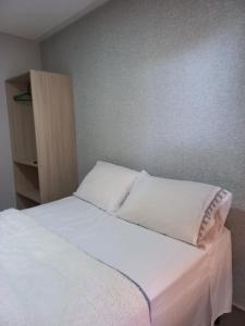 1 cama con sábanas blancas y almohadas en una habitación en Rosa dos ventos suíte 1, en Florianópolis