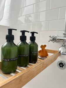 quatro garrafas verdes numa prateleira ao lado de um lavatório em Juniper House by Walpole Bay - Margate em Kent
