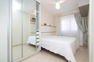 1 dormitorio con cama blanca y espejo en Aluguel Apartamento 2 quartos c/ 1 suíte | Bombas/SC, en Bombinhas