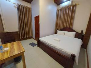 Habitación pequeña con cama y mesa de madera. en Inthavong Hotel/Guest House en Vang Vieng
