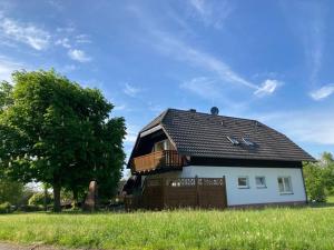 ein kleines weißes Haus mit einem Balkon und einem Baum in der Unterkunft Ferienhaus Moni mit 2 separaten Wohnungen am Silbersee in Frielendorf