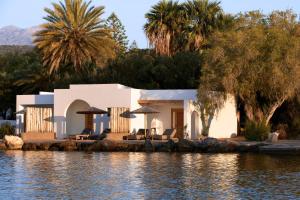 una casa junto al agua con sillas y sombrillas en Minos Beach Art Hotel, a Member of Design Hotels, en Agios Nikolaos