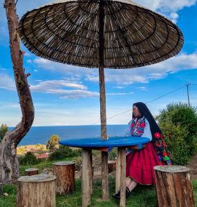 uma mulher sentada numa mesa debaixo de um guarda-chuva em Inca lodge - Amantani em Ocosuyo