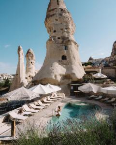 ギョレメにあるAza Cave Cappadocia Adult Hotelの椅子とパラソルが置かれたプールに座る女性