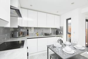 een witte keuken met witte kasten en een tafel bij Modern Home in Derby City Centre - Free Gated Parking in Derby