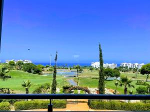 Blick auf einen Golfplatz mit Palmen und das Meer in der Unterkunft Asilah Marina Golf Appart Rez de Jardin Vue sur Mer in Asilah