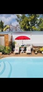 a pool with a red umbrella and two chairs and a table at Villa with pool close to the sea in Saint-Gilles les Bains