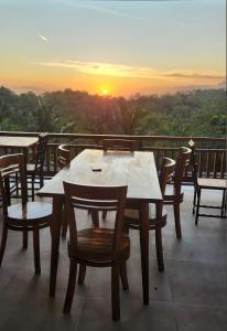 Kelingking Hostel في Klungkung: طاولة وكراسي على شرفة مع غروب الشمس