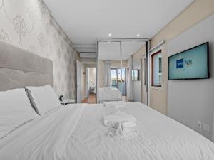 um quarto com uma cama branca e uma televisão na parede em Solar Encantado em Gramado