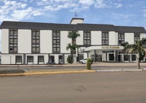 a large white building with palm trees in front of it at Hotel Plaza Sul in Caràzinho