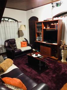 sala de estar con sofá de cuero y TV en Chalé de Férias, en Campos do Jordão