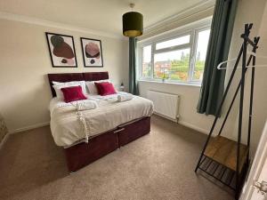 ein Schlafzimmer mit einem Bett mit roten Kissen und einem Fenster in der Unterkunft Tennyson House - Cul De Sac 3 Bedroom House for Families, Business Travellers, Contractors, Free Parking & Wifi, Nice Garden in Royal Wootton Bassett