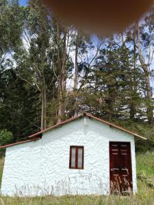 un hangar blanc avec portes rouges dans un champ dans l'établissement Casa Enverdes, à Guasca