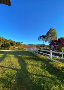 a pasture with a white fence and a red house at Casa de temporada - Recanto da invernada in Urubici