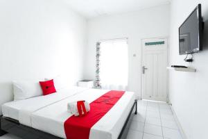 a white bedroom with a bed with red pillows and a tv at RedDoorz near Grojogan Sewu Tawangmangu in Karanganyar