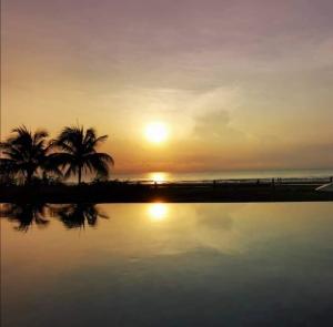 een zonsondergang met palmbomen en een waterlichaam bij Saqina Haven timurbay seafront residences in Kuantan