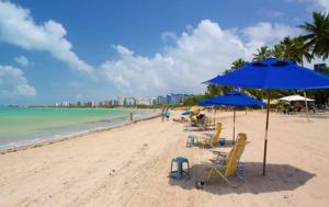 a beach with chairs and umbrellas and the ocean at Apartamento dúplex em frente ao mar de Pajuçara in Maceió