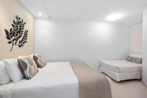 a white bedroom with a bed and a chair at Fairshore 12: Absolute Beachfront, Direct Beach & Pool Access in Noosa Heads +7 photos