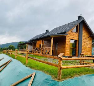 une cabane en rondins avec une clôture et de l'eau devant elle dans l'établissement Domki Oaza Ciszy, à Polańczyk