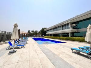 eine Reihe von Liegestühlen und Sonnenschirmen neben einem Pool in der Unterkunft PR25 - Cozy 1BR in Polo Residences in Dubai