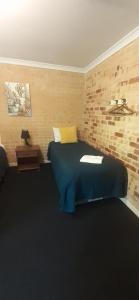 Un dormitorio con una cama azul y una pared de ladrillo en Travellers Rest Motel, en Mundaring