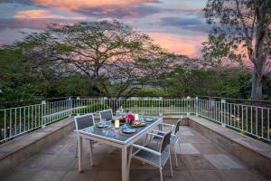 a table and chairs on a balcony with a sunset at ama Stays & Trails Helen's Garden , Bhopal in Bhopal