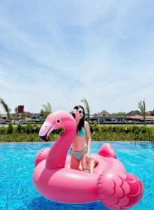 Uma mulher está sentada num flamingo cor-de-rosa numa piscina. em BAY RESORT HOI AN em Hoi An