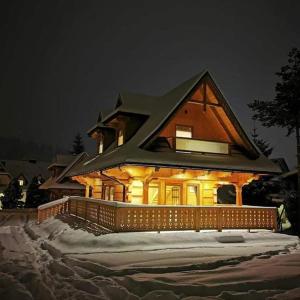 a house with lights on in the snow at night at Chaty Misiagi in Poronin