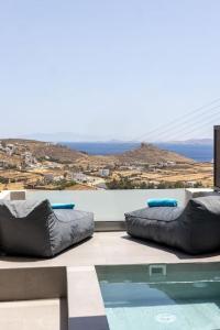 un balcón con 2 pufs y una piscina en Pearl Suites and Villa Tinos, en Tinos