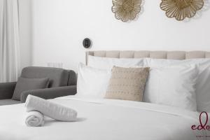 a white bed with white pillows and a chair at דירת סטודיו עם מרפסת במתחם סי סייד - By Edomlux in Eilat