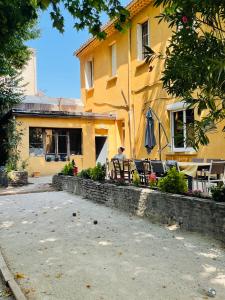 een man die op een bankje voor een geel gebouw zit bij La Maison TILIA in Bessèges