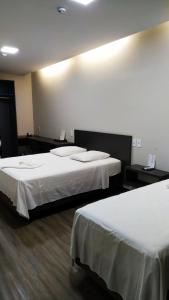 two beds in a hotel room with white sheets at Hotel Barril in Primavera do Leste