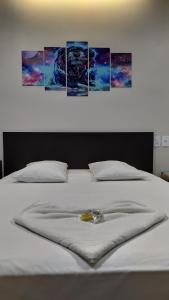 a white bed with four paintings on the wall at Hotel Barril in Primavera do Leste