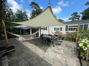 a patio with a tent and hammocks in front of a house at Forest Family 6 persoons op 5 sterren park in Beekbergen