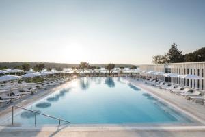 una gran piscina con tumbonas y sombrillas en Falkensteiner Hotel Park Punat en Punat