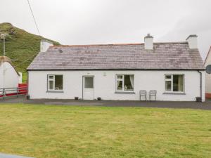 a white house with two chairs in a yard at Maghera Caves Cottage in Ardara