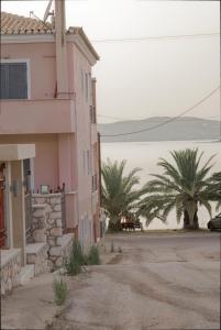 um edifício cor-de-rosa com palmeiras ao fundo em Niriides Apartments em Porto Heli