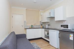 una cocina con armarios blancos y un sofá. en Evergreen Apartments- Flat 1, London, en Londres