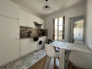 - une cuisine avec une table, des armoires blanches et un lave-linge dans l'établissement Le Monterelais : Hypercentre, à Montereau-faut-Yonne