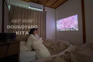 een vrouw op een bed in een slaapkamer met een tv bij GUEST HOUSE DOUGOYADO KITA - Vacation STAY 14923 in Matsuyama