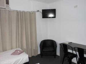 Habitación con cama, silla y TV en la pared. en Parkway Motel, en Queanbeyan