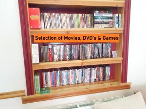 a book shelf filled with dvds and games at F1 MAISON 108 - Holiday Home - Full Kitchen - Street FREE PARKING, NETFLIX - 68Mbps BT WIFI - DVD's - Welcome Tray - By Corner from Gavin n Stacey Film House in Barry