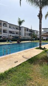 - une piscine en face d'un bâtiment avec un palmier dans l'établissement Mohammédia Marbella beach appartement familliale, à Minaret de Mansuria