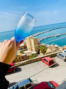 eine Person, die ein blaues Glas vor einer Stadt hält in der Unterkunft Holiday Marty&kalos in Sciacca