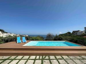 una piscina con due sedie blu e l'oceano di Villa capri con giardino e piscina a Capri