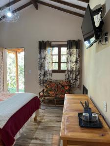 a bedroom with a bed and a table and a tv at Pousada Recanto dos Pássaros in Cunha