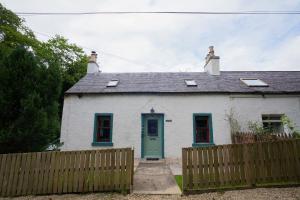 ein weißes Haus mit blauer Tür und einem Zaun in der Unterkunft Tig Cottage - a rural, quirky, pet friendly 2 bedroom cottage near Ballantrae in Ballantrae