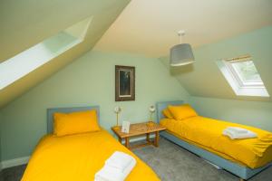 two beds in a room with yellow sheets and a table at Tig Cottage - a rural, quirky, pet friendly 2 bedroom cottage near Ballantrae in Ballantrae