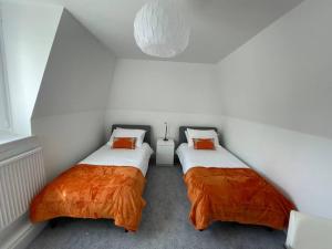 Cette chambre comprend 2 lits dans une chambre dotée de murs blancs et d'oreillers orange. dans l'établissement Fantastic home in Brightons, Falkirk., à Polmont