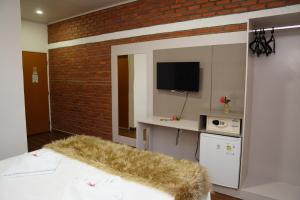 1 dormitorio con 1 cama, TV y pared de ladrillo en Pedra do Sino Hotel, en Piranhas